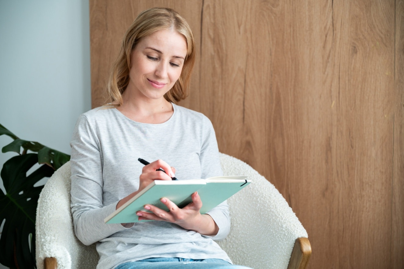 A woman smiles while writing in her journal for mental health in a calm space