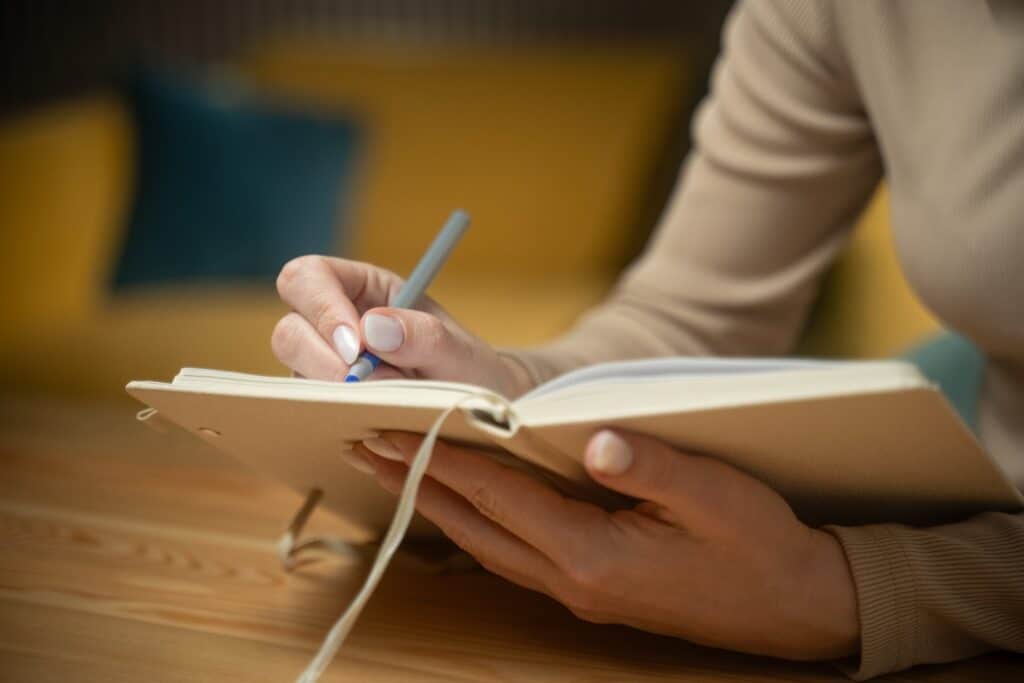 Close-up of hands writing in a journal for mental health on a wooden table