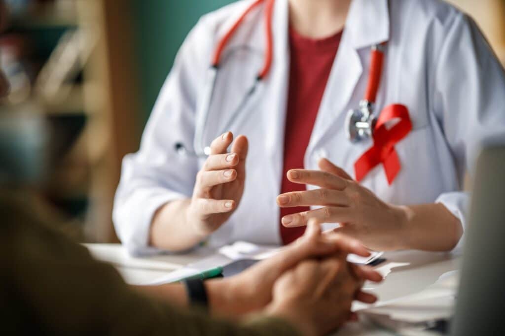 A patient listens to a doctor’s diagnosis for AIDS. The red ribbon symbolizes HIVAIDS awareness.