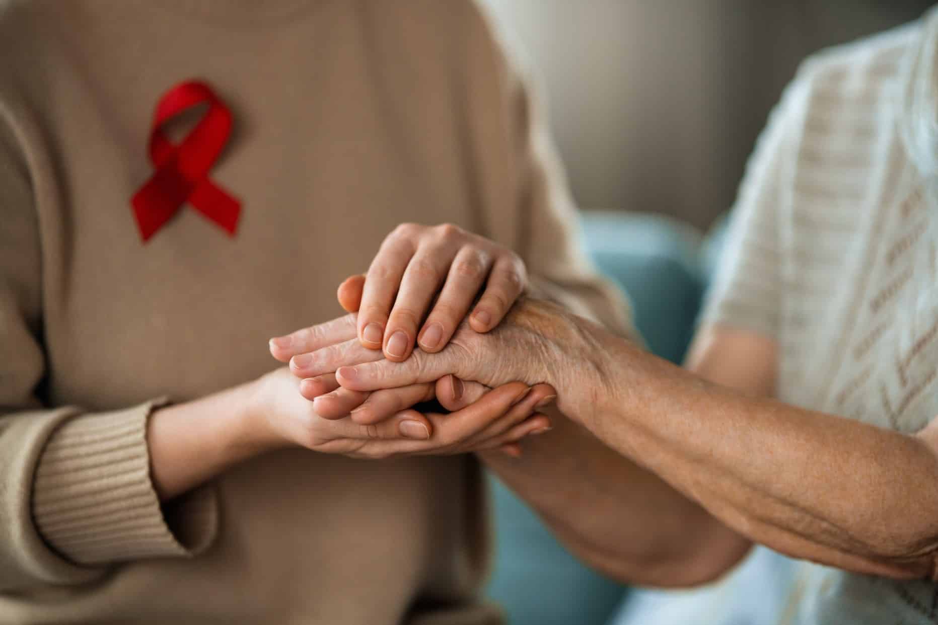 A woman holding another’s hand in support of HIV. The red ribbon symbolizes HIVAIDS awareness.