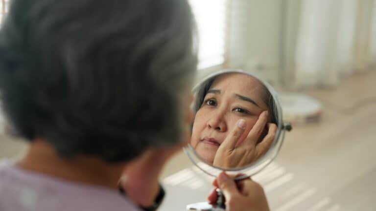 Woman looking in a mirror at her face, wondering what causes rapid aging in her skin