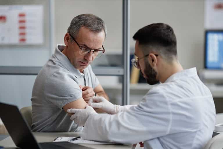 Doctor examining the upper arm of a middle-aged male patient during a supervised testosterone evaluation in Bangkok.