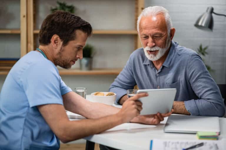 A clinician reviews a tablet with an older male patient during a consultation.