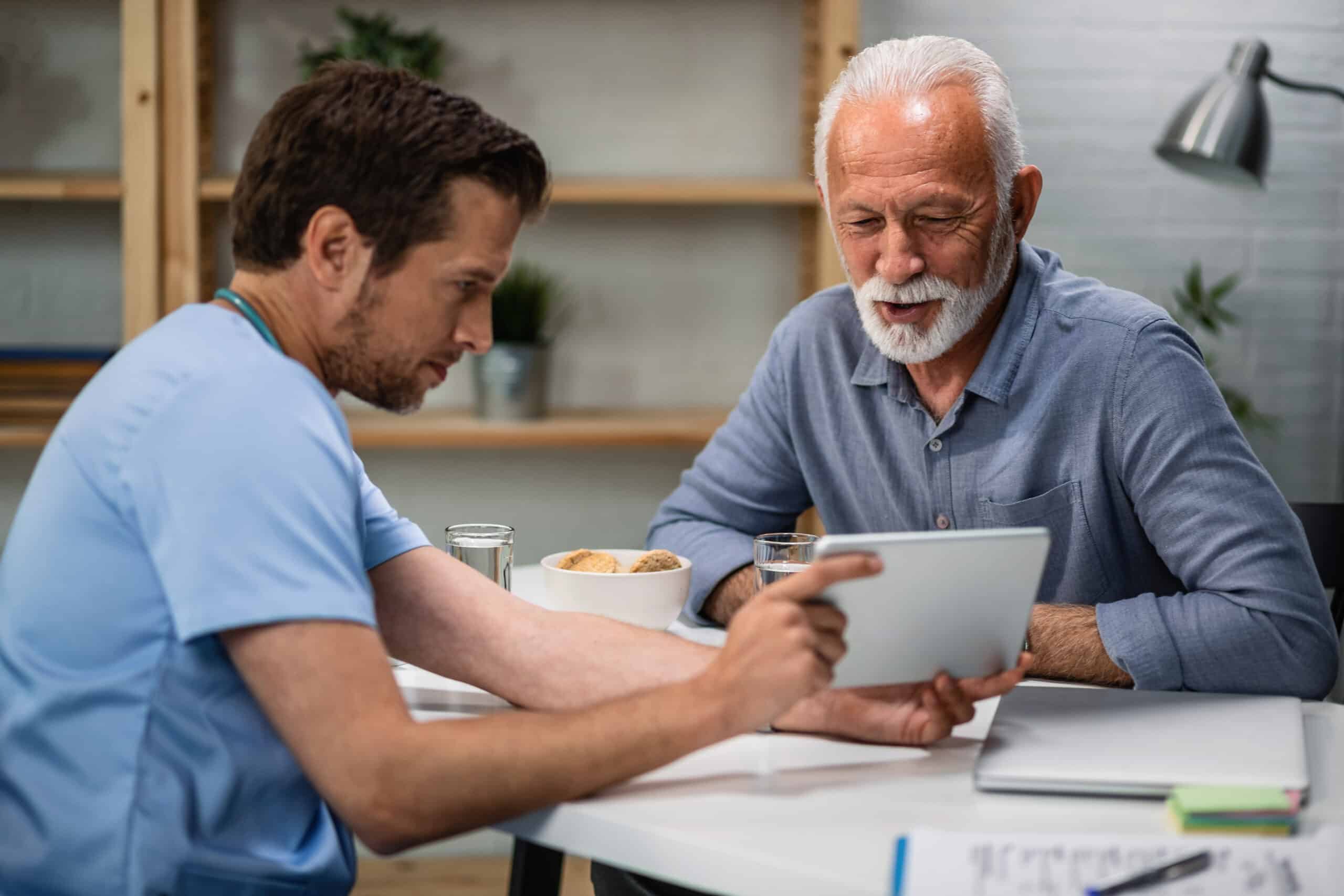 A clinician reviews a tablet with an older male patient during a consultation.