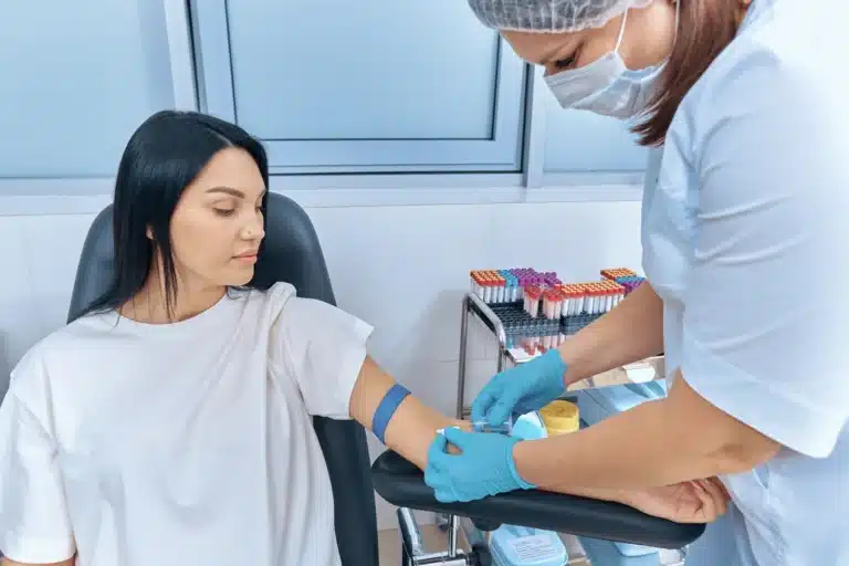 Woman having a blood sample collected by a healthcare professional wearing gloves.