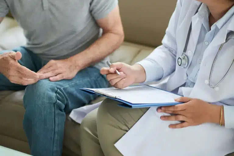 Doctor taking notes during a consultation with a male patient.